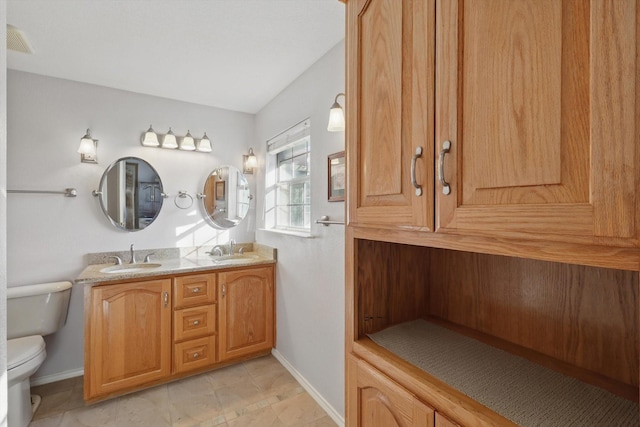 bathroom featuring toilet, double vanity, a sink, and baseboards