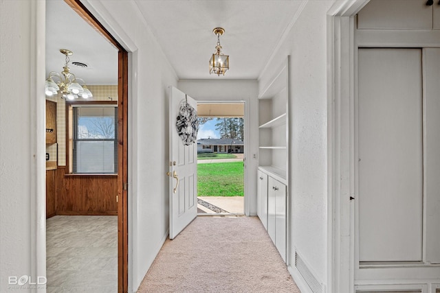 interior space featuring a notable chandelier, a textured wall, ornamental molding, light carpet, and wooden walls