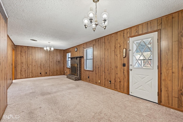 unfurnished living room with a textured ceiling, wooden walls, light colored carpet, a notable chandelier, and a fireplace