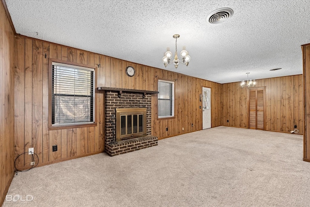 unfurnished living room with a textured ceiling, a notable chandelier, light carpet, a fireplace, and visible vents