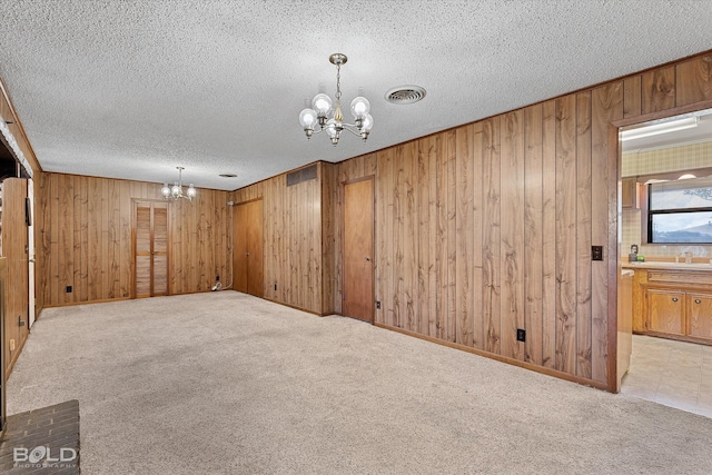 spare room featuring light carpet, visible vents, a chandelier, and a textured ceiling