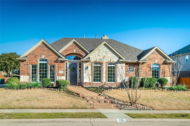 view of front of house with brick siding, a chimney, a shingled roof, a front yard, and stone siding