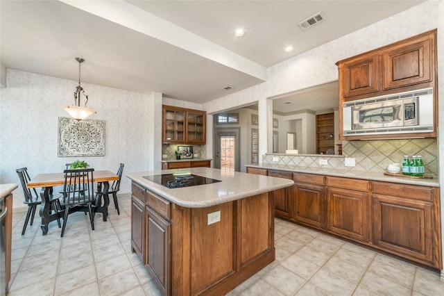 kitchen featuring visible vents, a kitchen island, stainless steel microwave, black electric stovetop, and light countertops