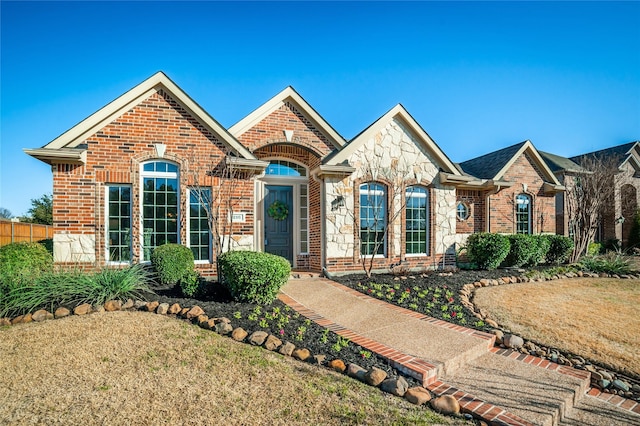 view of front of house with stone siding, a front yard, fence, and brick siding