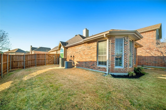 back of property with a yard, a fenced backyard, a chimney, and brick siding