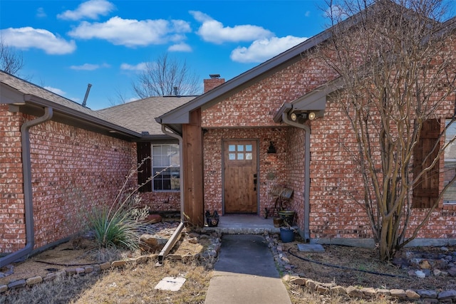 doorway to property with a garage, a shingled roof, a chimney, and brick siding