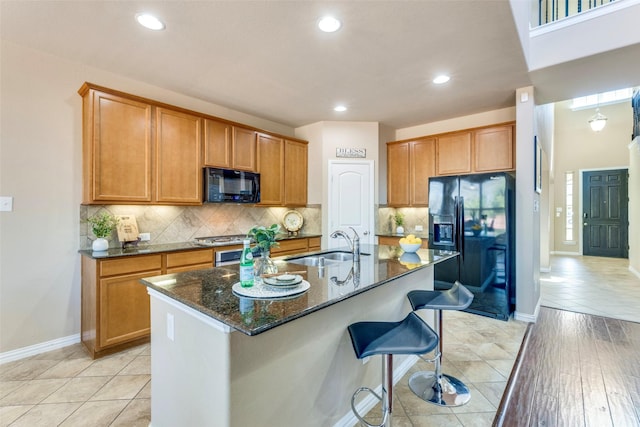 kitchen with decorative backsplash, dark stone counters, a kitchen breakfast bar, black appliances, and a sink