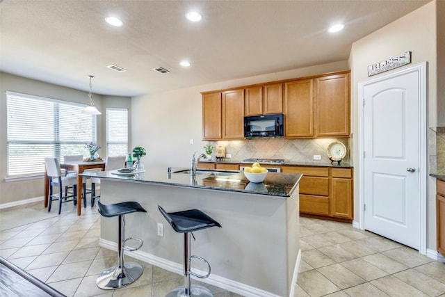 kitchen featuring black microwave, light tile patterned floors, a sink, and decorative backsplash