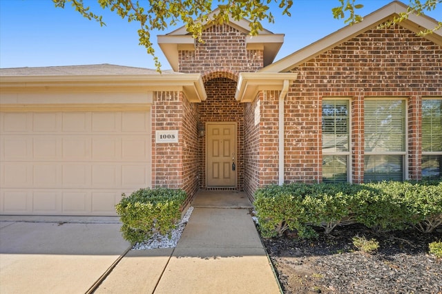 view of exterior entry with an attached garage and brick siding