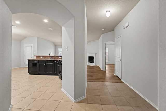 hallway with arched walkways, light tile patterned floors, vaulted ceiling, a sink, and baseboards