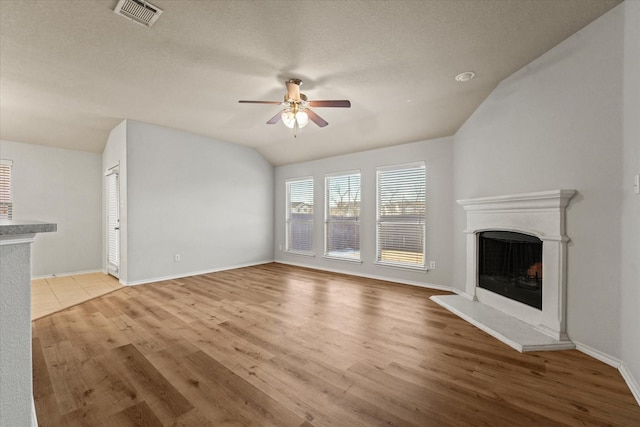 unfurnished living room with visible vents, a fireplace with raised hearth, a ceiling fan, light wood-style flooring, and vaulted ceiling