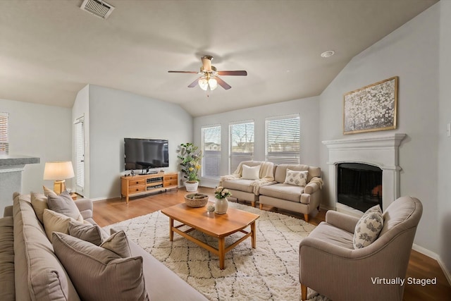 living area with visible vents, a ceiling fan, lofted ceiling, wood finished floors, and a fireplace