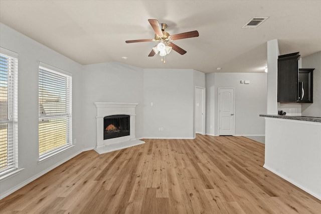 unfurnished living room with visible vents, a fireplace with raised hearth, ceiling fan, wood finished floors, and baseboards