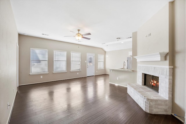 unfurnished living room featuring baseboards, visible vents, dark wood finished floors, a ceiling fan, and a brick fireplace