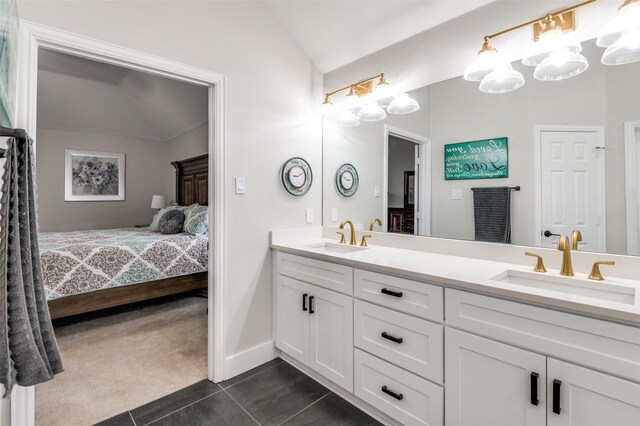 ensuite bathroom featuring lofted ceiling, tile patterned flooring, a sink, and double vanity