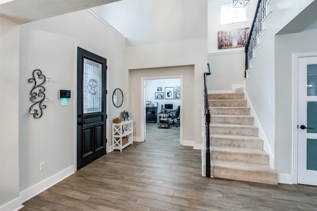 foyer entrance with baseboards, a high ceiling, stairway, and wood finished floors