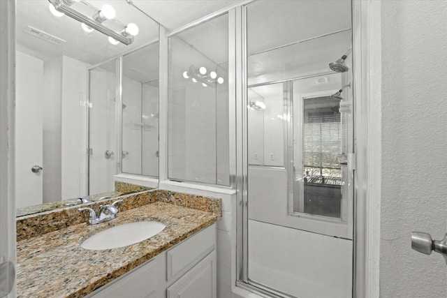 full bathroom with a stall shower, a textured wall, visible vents, and vanity