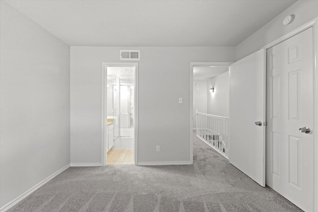 unfurnished bedroom with light carpet, connected bathroom, visible vents, and baseboards