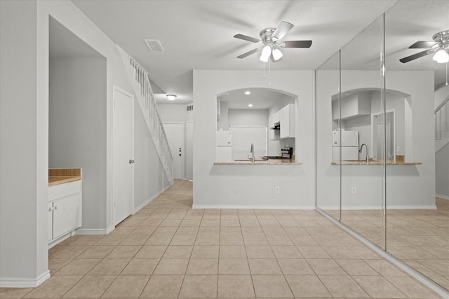 unfurnished living room with visible vents, ceiling fan, stairs, a sink, and light tile patterned flooring