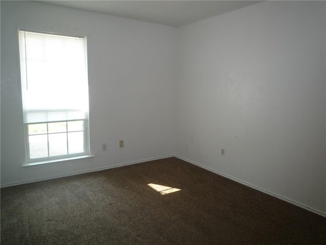 unfurnished room featuring dark carpet and baseboards