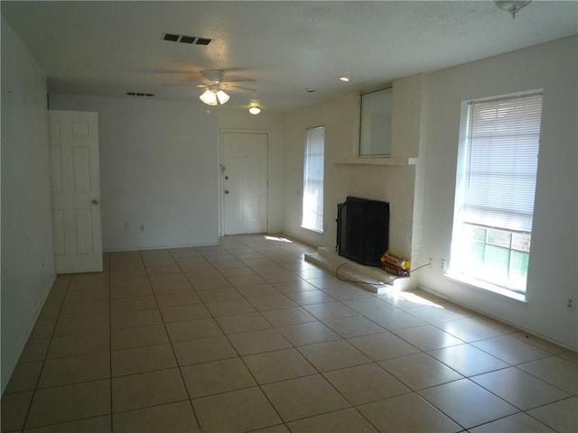 unfurnished living room with light tile patterned floors, a fireplace with raised hearth, visible vents, and a ceiling fan