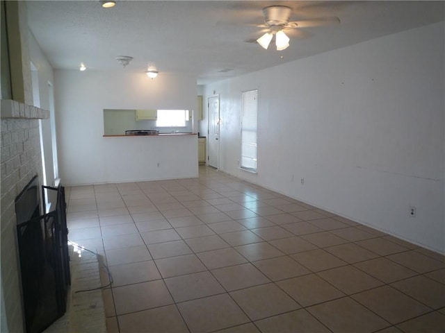 unfurnished living room with a brick fireplace, ceiling fan, and light tile patterned flooring