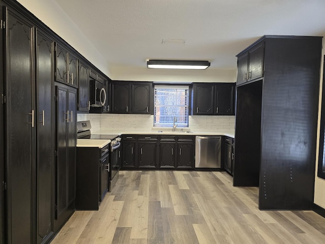 kitchen featuring light wood-type flooring, dark cabinets, stainless steel appliances, and a sink