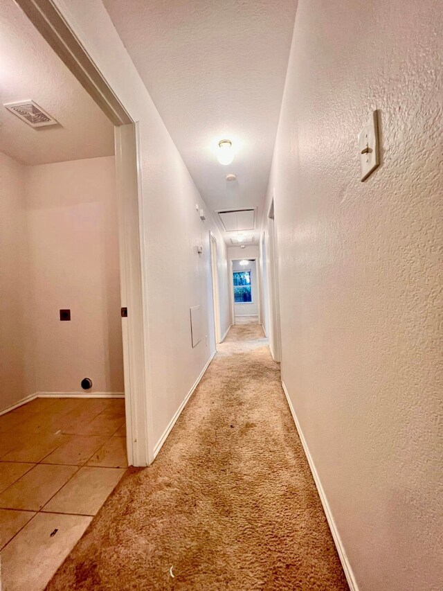 corridor featuring a textured wall, light carpet, visible vents, baseboards, and attic access