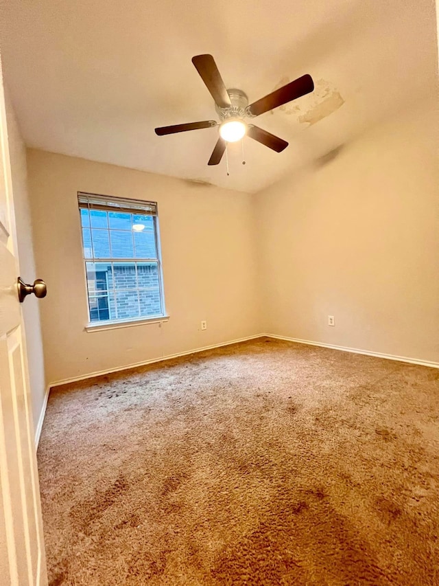 carpeted spare room featuring ceiling fan and baseboards