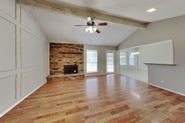 unfurnished living room with a ceiling fan, light wood-style flooring, vaulted ceiling with beams, a textured ceiling, and a fireplace