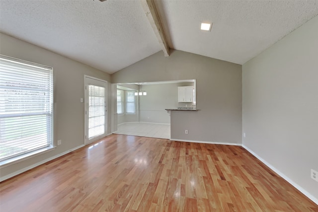 unfurnished living room with light wood-type flooring, vaulted ceiling with beams, baseboards, and a textured ceiling