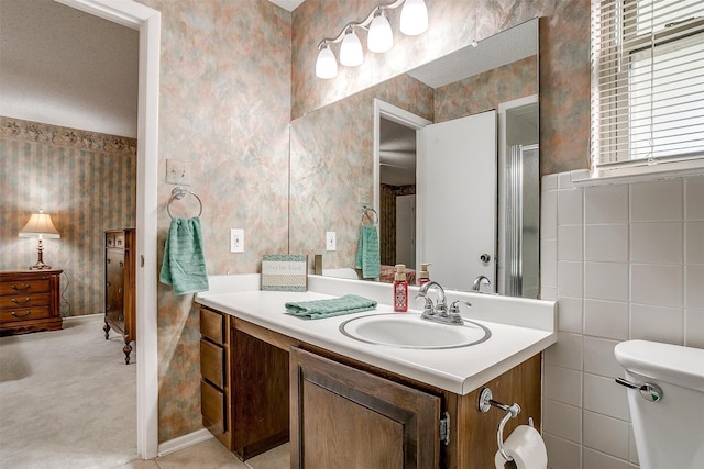 bathroom with toilet, tile walls, vanity, and wallpapered walls