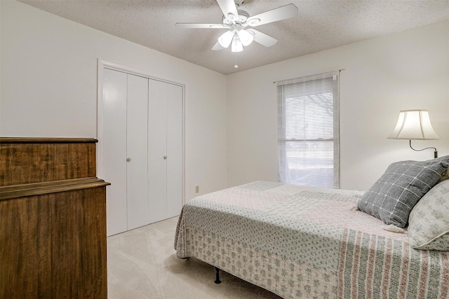 bedroom featuring a ceiling fan, a closet, light colored carpet, and a textured ceiling