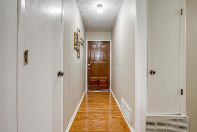 doorway with baseboards, light wood-style flooring, visible vents, and a textured ceiling