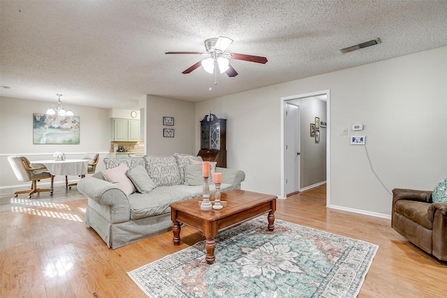 living room featuring ceiling fan with notable chandelier, light wood-style flooring, a textured ceiling, and visible vents