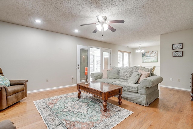 living area featuring recessed lighting, a textured ceiling, light wood-type flooring, baseboards, and ceiling fan with notable chandelier