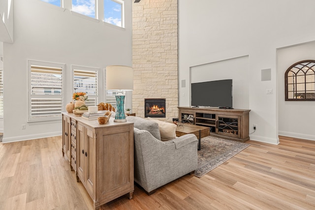 living room featuring a high ceiling, a fireplace, light wood-style flooring, and baseboards