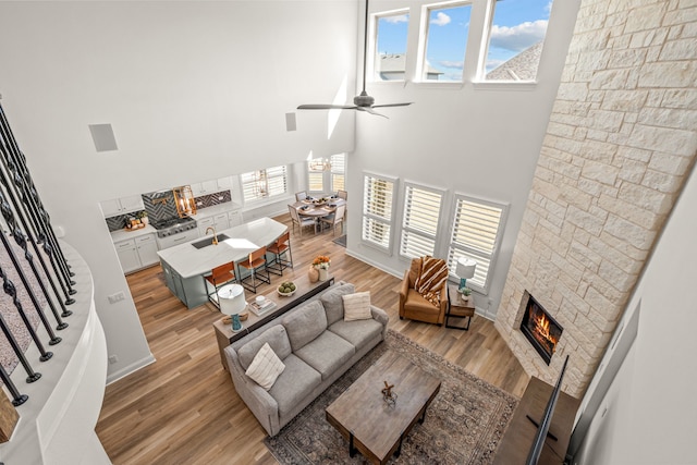 living area with stairway, a fireplace, light wood-style flooring, and a high ceiling