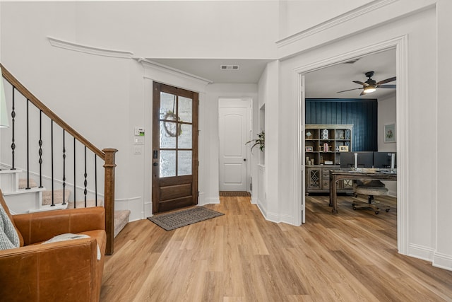 foyer with ornamental molding, light wood-type flooring, visible vents, and stairway