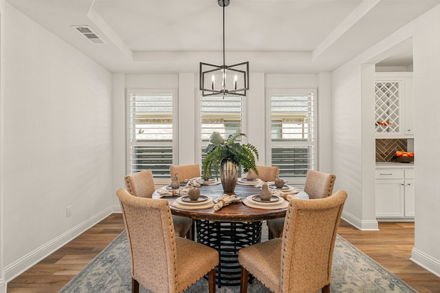 dining area featuring plenty of natural light, visible vents, a raised ceiling, and wood finished floors