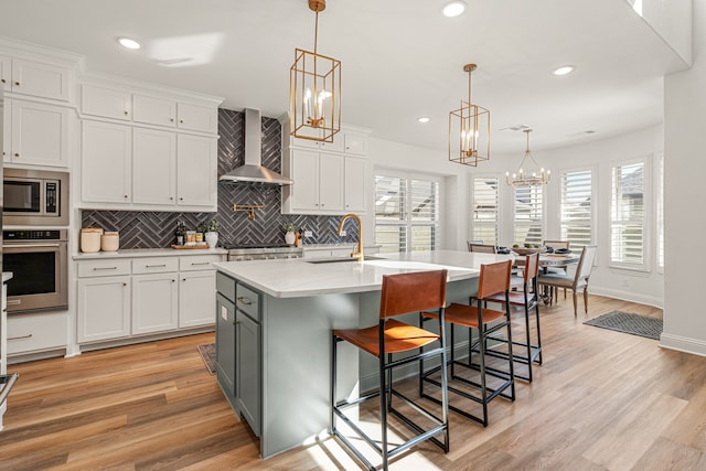 kitchen featuring a sink, white cabinets, light countertops, wall chimney range hood, and appliances with stainless steel finishes