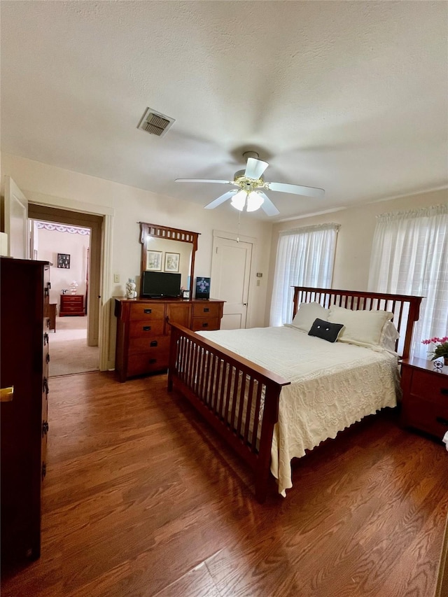 bedroom with a ceiling fan, a textured ceiling, visible vents, and wood finished floors