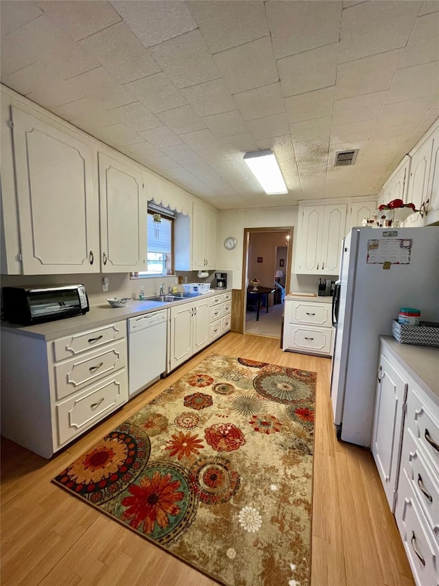 kitchen with white appliances, visible vents, white cabinetry, and light wood finished floors