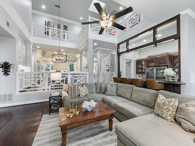 living room featuring ceiling fan with notable chandelier, a high ceiling, wood finished floors, and visible vents