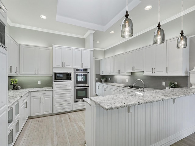 kitchen with light wood-type flooring, appliances with stainless steel finishes, white cabinets, and ornamental molding