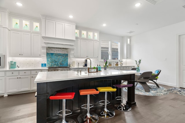 kitchen with tasteful backsplash, a center island with sink, glass insert cabinets, and white cabinetry