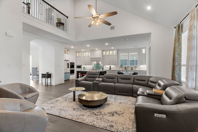 living area with dark wood-type flooring, arched walkways, plenty of natural light, and ceiling fan