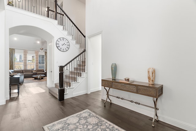 entrance foyer with stairway, a high ceiling, arched walkways, and dark wood-style flooring