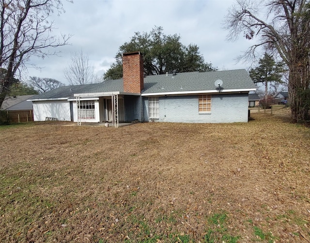 back of house featuring brick siding, a yard, a chimney, and fence