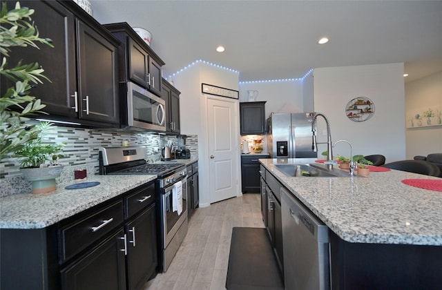 kitchen with light wood finished floors, decorative backsplash, a kitchen island with sink, stainless steel appliances, and a sink